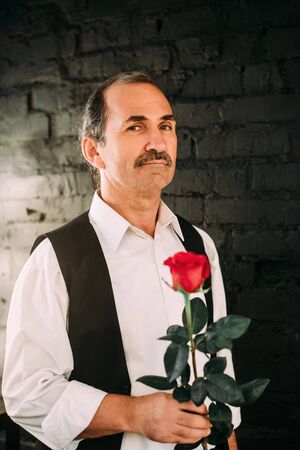 Handsome middle aged man is dressed in a white shirt and a black vest. Black background.の写真素材