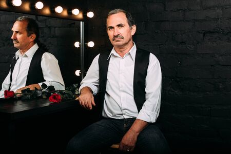 Handsome middle aged man is dressed in a white shirt and a black vest. Black background.