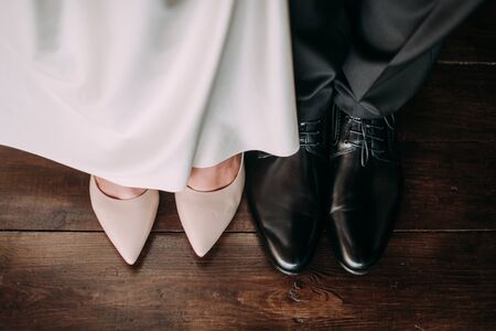 Love and happiness on wedding day. Closeup of bride's and groom's feet and shoes and wooden decoration 'love' in their hands.の写真素材