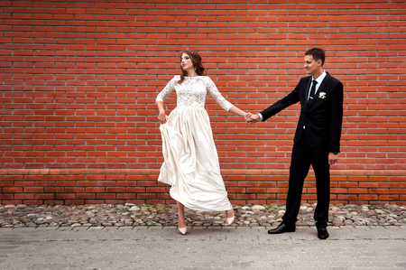Newlyweds embracing next to red brick wall. Young wedding couple.の写真素材