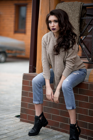 Spring in the country style. Full length portrait of young woman in white knitted sweater and furry hat standing in the front of rustic wood wall in the yard near house, wearing sweaterの写真素材