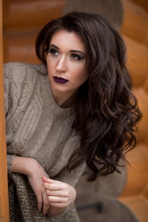 Spring in the country style. Full length portrait of young woman in white knitted sweater and furry hat standing in the front of rustic wood wall in the yard near house, wearing sweaterの写真素材