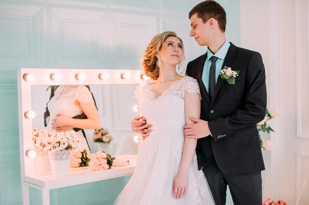 Happy couple. Wedding photo shoot in the white studio with wedding decor kisses, hugs. On the background of make up mirrorの写真素材