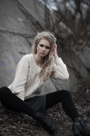 Close up of beautiful young  blonde woman with blue eyes in white pullover, sitting.
Winter, spring, outdoor portrait. Professional beauty make-up: dark smoky eyes and pale lips and hair style.の写真素材