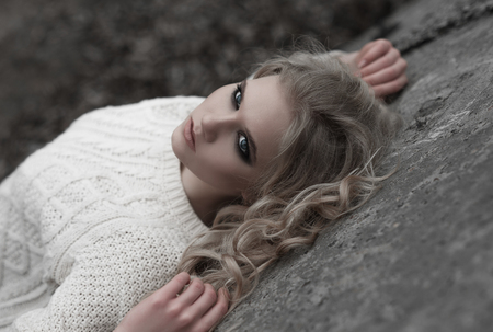 Close up of beautiful young  blonde woman with blue eyes in white pullover. 
Winter, spring, outdoor portrait. Professional beauty make-up: dark smoky eyes and pale lips and hair style.の写真素材