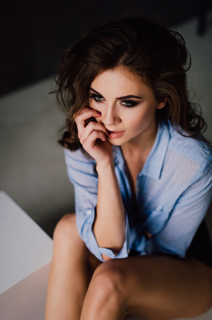 Portrait of sexy young woman posing in studio at natural light, wearing blue shirt, has good and healthy fitの写真素材