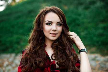 Beautiful young hipster girl posing and smiling near urban wall background in red plaid shirt, shorts, outdoors summer portrait.の写真素材