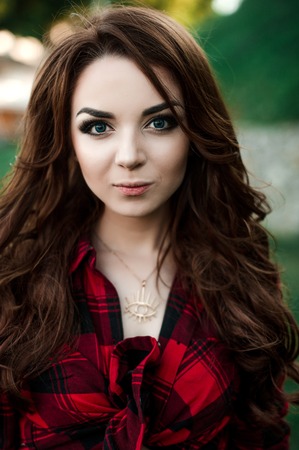 Beautiful young hipster girl posing and smiling near urban wall background in red plaid shirt, shorts, outdoors summer portrait.の写真素材