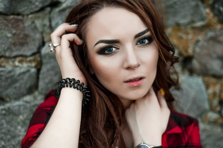 Beautiful young hipster girl posing and smiling near urban wall background in red plaid shirt, shorts, outdoors summer portrait.の写真素材