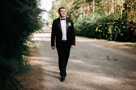 Elegant young happy wedding couple is sitting at green grass on green sunny summer background near the white canopy hugging, smiling and kissing.の写真素材