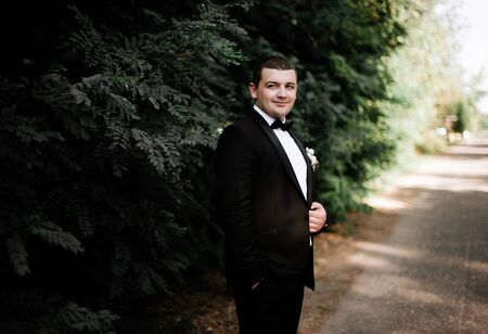 Elegant young happy wedding couple is sitting at green grass on green sunny summer background near the white canopy hugging, smiling and kissing.の写真素材