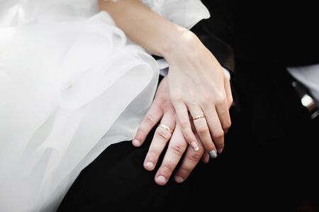 Elegant young happy wedding couple is sitting at green grass on green sunny summer background near the white canopy hugging, smiling and kissing.の写真素材