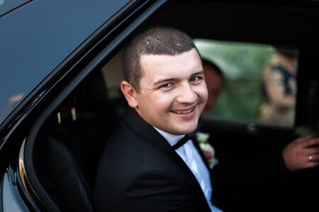 Elegant young happy wedding couple is sitting at green grass on green sunny summer background near the white canopy hugging, smiling and kissing.の写真素材