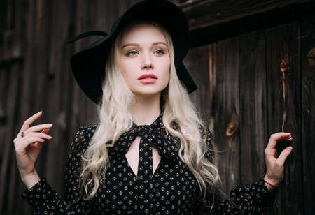 Beautiful attractive and stylish girl wearing black hat standing posing in city. Nude makeup, best daily hairstyle and great fashion glamour country style.の写真素材