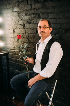 Handsome middle aged man is dressed in a white shirt and a black vest. Black background.の写真素材