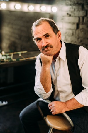 Handsome middle aged man is dressed in a white shirt and a black vest. Black background.の写真素材