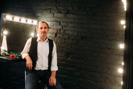 Handsome middle aged man is dressed in a white shirt and a black vest. Black background.の写真素材