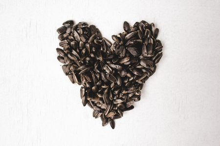 Black sunflower bird seed forms a heart shape on white background.の写真素材