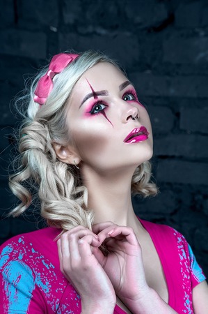 Beautiful blonde girl with two pigtails, with creative make-up: pink glossy lips, wearing pink...