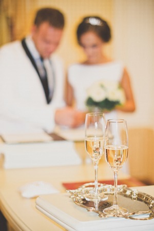 Wedding glasses are in the foreground. Blurred outlines newlyweds seen in the background.の写真素材