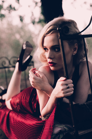 Beautiful and elegant blonde woman with red lips and hair waves wearing wine red nightie posing on...