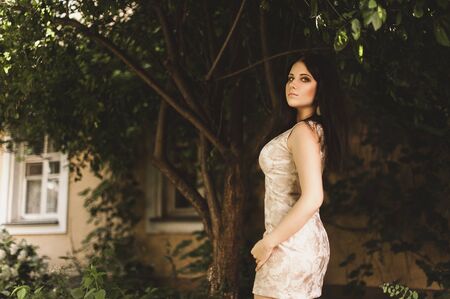 Beautiful young woman sexy brunette girl with make-up courtyard, dressed in light dress, pleasure spring summer nature sunny warm morning smileの写真素材