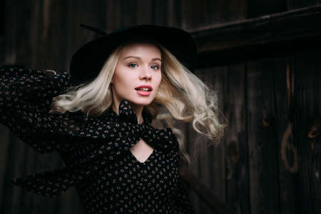 Beautiful attractive and stylish girl wearing black hat standing posing in city. Nude makeup, best daily hairstyle and great fashion glamour country style.の写真素材