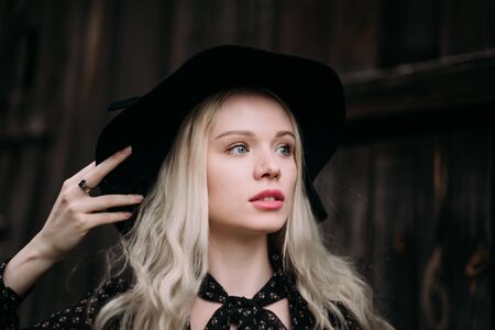 Beautiful attractive and stylish girl wearing black hat standing posing in city. Nude makeup, best daily hairstyle and great fashion glamour country style.の写真素材