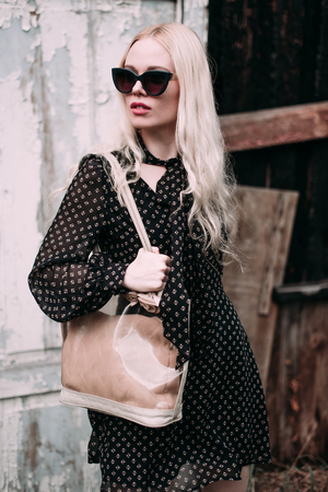Beautiful blonde young woman wearing sunglasses,black top and pencil skirt, hat and handbag, standing on the street. Fashion photoの写真素材