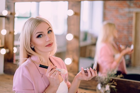 Portrait of a beautiful blonde woman applying makeup near a mirror.の写真素材