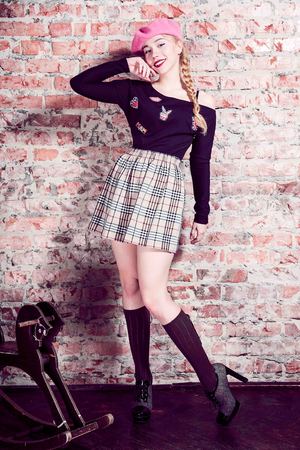 Fashion shot of a blonde girl wearing modern youth clothes. College, school style. Hipster girl wearing glasses by a brick wall. Youth fashionの写真素材