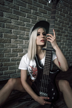 Young European teenage brunette  model ,  wearing blue jeans mini shorts, sneakers, and black t-shirt, posing with a guitarの写真素材