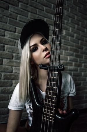 Young European teenage brunette  model ,  wearing blue jeans mini shorts, sneakers, and black t-shirt, posing with a guitarの写真素材
