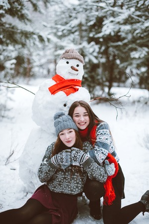 Two young teenage hipster girl friends together.Close up fashion portrait of two sisters hugs and having fun winter time,wearing sweater,best friends couple outdoors, snowy weatherの写真素材