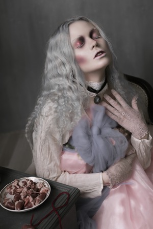 Dark halloween portrait of scary bad zombie girl sitting in a chair and collecting hearts. Conceptual photoの写真素材