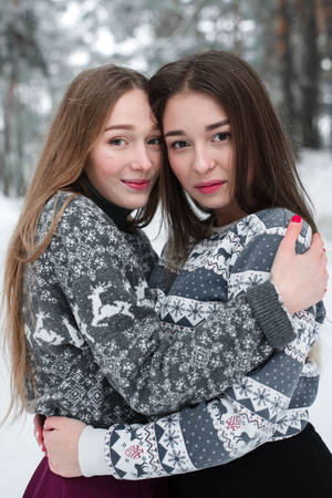 Two young teenage hipster girl friends together.Close up fashion portrait of two sisters hugs and having fun winter time,wearing sweater,best friends couple outdoors, snowy weatherの写真素材