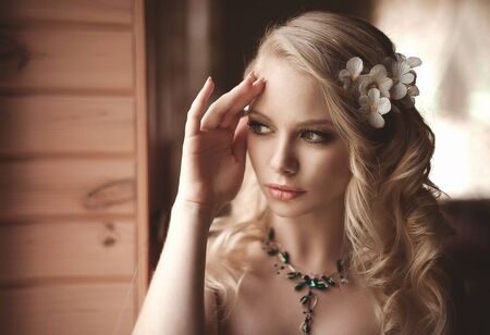 Young beautiful blonde in the bed at morning time near window under Sun rays with flower in the hair. Tender romantic moodの写真素材