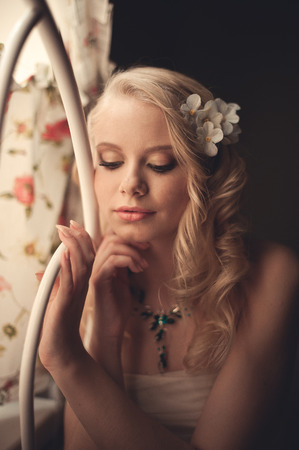 Young beautiful blonde in the bed at morning time near window under Sun rays with flower in the hair. Tender romantic moodの写真素材