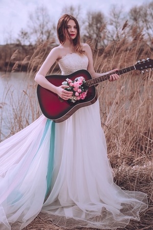 Beautiful romantic european girl with guitar with flowers inside, posing outdoors. Concept of music...