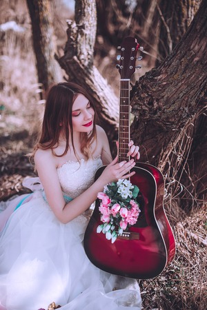 Beautiful romantic european girl with guitar with flowers inside, posing outdoors. Concept of music and nature. Spring time. Fashion retouched shotの写真素材