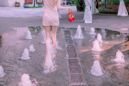 Beautiful young blond woman with hair in a dress near a fountain in a summer dayの写真素材