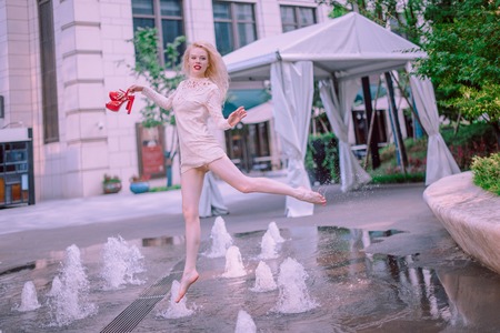Beautiful young blond woman with hair in a dress near a fountain in a summer dayの写真素材