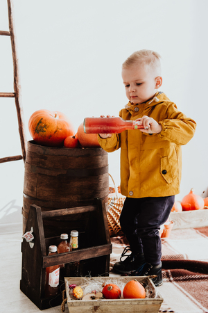 Cool trendy hipster boy 2 years old wears yellow jacket posing at the decorated photozone of autumn decor with beautiful bright autumn leaves. Cosy atmosphereの写真素材