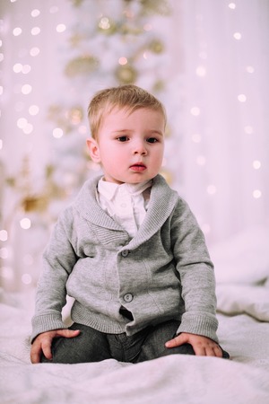 Cheerful little baby boy playing near Christmas tree, gold and beige pastel cの写真素材