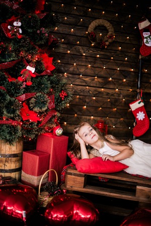 Baby girl 4-5 year old posing in room over christmas tree with decorations. Looking at camera. Merry christmas. Wearing stylish dress.の写真素材