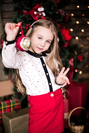 Baby girl 4-5 year old posing in room over christmas tree with decorations. Looking at camera. Merry christmas. Wearing stylish dress.の写真素材