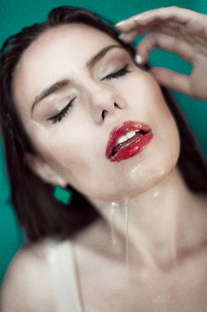 Close-up of beautiful wet woman face with water drop. On green backgroundの写真素材