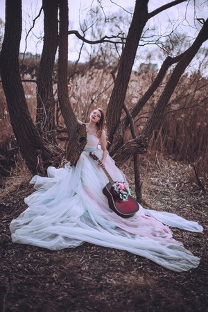 Beautiful romantic european girl with guitar with flowers inside, posing outdoors. Concept of music and nature. Spring time. Fashion retouched shotの写真素材