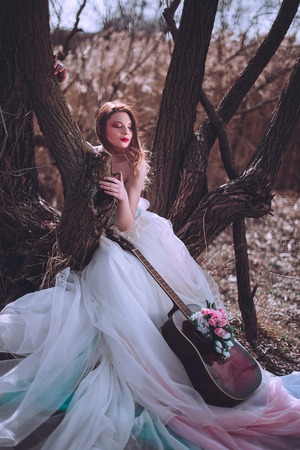 Beautiful romantic european girl with guitar with flowers inside, posing outdoors. Concept of music and nature. Spring time. Fashion retouched shotの写真素材
