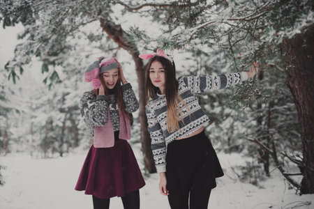 Two young teenage hipster girl friends together.Close up fashion portrait of two sisters hugs and having fun winter time,wearing sweater,best friends couple outdoors, snowy weatherの写真素材